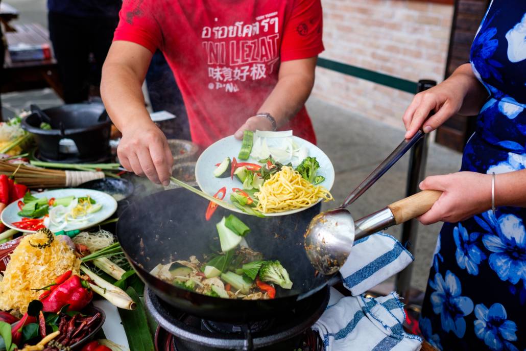 image of two people putting ingredients in a wok