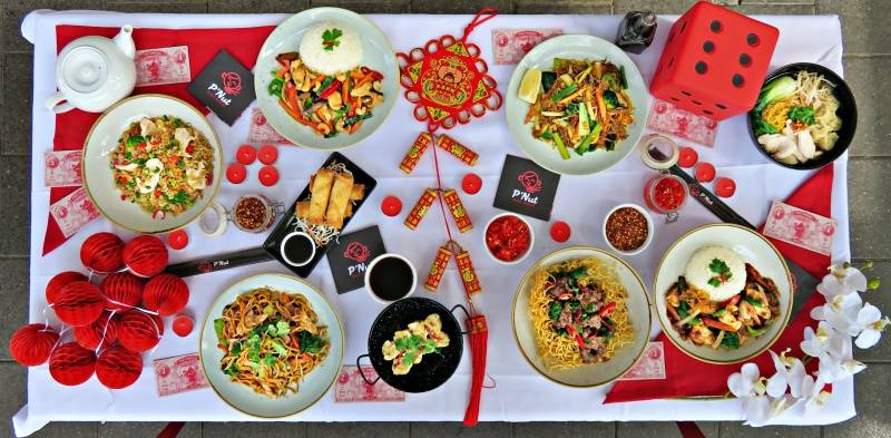 A table setting as seen from above. The table is filled with red decorations and Chinese food.